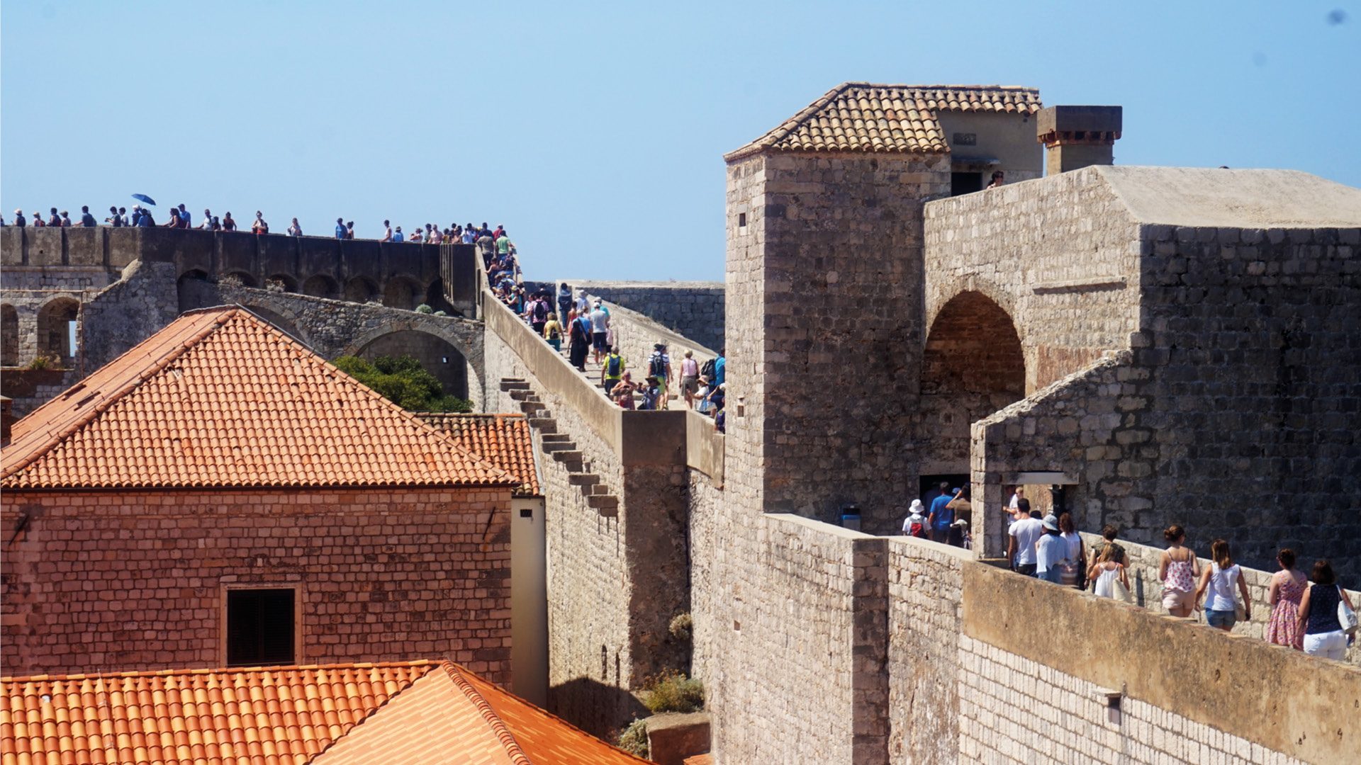 Een bezoek aan Dubrovnik is pas compleet wanneer je een wandeling over de spectaculaire stadsmuren hebt gemaakt. Ze vertellen het geschiedenisverhaal van Dubrovnik en geven je een unieke kijk in het verleden van de stad. De stadsmuren staan al sinds 1979 op de UNESCO Werelderfgoedlijst. Kom meer te weten over de historie van Dubrovnik en haar stadsmuren. Een stukje geschiedenis voor je vertrekt De muren en forten van Dubrovnik hebben door de eeuwen heen een belangrijke verdedigende rol gespeeld voor Dubrovnik. Ook tijdens de meest recente oorlog (1991/1992) liepen de oude stad en de stadsmuren veel schade op. Dubrovnik is in de 7e eeuw gesticht do or de inwoners van het stadje Epidaurum (nu Cavtat), zij waren op de vlucht voor binnenvallende slaven. Ze noemden de stad Ragusa. De Slavische naam voor de stad werd Dubrovnik. Na een tijd onder het Byzantijnse Rijk te hebben geleefd kwam Ragusa onder Venetiaans bestuur. Uiteindelijk werd Ragusa, bij de Vrede van Zadar (1359), onderdeel van Hongarije. Ragusa werd wel volledig zelf besturend en werd dus een vrije stadstaat. Gevolg: De stad werd ommuurd en voorzien van twee havens in Ragusa en Cavtat. De republiek breidde haar grondgebied steeds meer uit. Een einde aan de bloeiperiode van Ragusa Het hoogtepunt van de macht werd bereikt in de 15e en 16e eeuw. De zeemacht was op dat moment net zo machtig als die van Venetië en andere Italiaanse zeestaten. Echter kwam hier ook het keerpunt. Ragusa ondersteunde het Ottomaanse Rijk tegen de Portugezen tijdens de Slag van Diu. Deze slag werd verloren door het Ottomaanse Rijk, waardoor de handelsroute zich verplaatste van de Middellandse Zee naar Indië (dat was in handen van Portugal). De handelscrisis en een rampzalige aardbeving in 1667 maakten een einde aan de bloeiperiode van Ragusa. In 1699 bij de Vrede van Karlowitz werden er twee kleine grensgebieden van Ragusa geschonken aan het Ottomaanse Rijk. Dit om op die manier te voorkomen dat Venetië (in die tijd de grootste bedreiging voor Ragusa) via land Ragusa kon aanvallen. Als gevolg van dit verdrag maakt het kustplaatsje Neum tegenwoordig nog steeds deel uit van Bosnië en Herzegovina. Momenteel is dit plaatsje dus nog steeds een onderbreking in het Kroatische grondgebied. Tijdens de Kroatische onafhankelijkheidsoorlog Ragusa gaf zich over aan de Fransen in 1806 om een Russisch-Montenegrijnse belegering te beëindigen. Hierdoor werd de stad gered, maar in 1808 schafte de maarschalk Marmont de republiek af. Na WO I werd het gebied een deel van Joegoslavië. In 1991, gedurende de Kroatische onafhankelijkheidsoorlog, werd het historisch centrum en de stadsmuren zwaar beschadigd door het Joegoslavische leger. Door het Joegoslavië Tribunaal werd deze daad gekwalificeerd als oorlogsmisdaad. De commandant Pavle Strugar werd dan ook veroordeeld tot 7,5 jaar gevangenisstraf. Praktische informatie Een wandeling duurt ongeveer 2 tot 3 uur, afhankelijk van het aantal stops dat je zelf inlast. Onderweg zijn er namelijk een aantal cafés waar je wat kan drinken. De lengte van de hele tocht is ongeveer 2 kilometer. Smeer je goed in Aangezien je over stadsmuren loopt kom je weinig schaduwplekken tegen. Zorg dus zeker dat je zonnebrand en water meeneemt. Op een aantal punten vind je restaurantjes waar je iets kan drinken. Op hete zomerdagen is de beste tijd voor een wandeling ‘s ochtends rond 11 uur of ‘s middags na 5 uur. Openingstijden en entreeticket Dubrovnik stadsmuren 2017/2018 Januari t/m februari: 10u t/m 15u Maart t/m 31 maart: 9u t/m 15u April t/m 31 mei: 9u t/m 18:30u Juni t/m 31 juli: 8u t/m 19:30u Augustus t/m 15 september: 8u t/m 19u 16 september t/m 31 oktober: 9u t/m 18u November t/m 31 december: 9u t/m 15u Entreeticket: Volwassenen: 150 HRK (ongeveer 20 euro) Kinderen: 50 HRK (ongeveer 7 euro) Kinderen onder de 5 jaar gratis De hoofdingang vind je bij de Pile Gate.