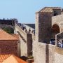 Een bezoek aan Dubrovnik is pas compleet wanneer je een wandeling over de spectaculaire stadsmuren hebt gemaakt. Ze vertellen het geschiedenisverhaal van Dubrovnik en geven je een unieke kijk in het verleden van de stad. De stadsmuren staan al sinds 1979 op de UNESCO Werelderfgoedlijst. Kom meer te weten over de historie van Dubrovnik en haar stadsmuren. Een stukje geschiedenis voor je vertrekt De muren en forten van Dubrovnik hebben door de eeuwen heen een belangrijke verdedigende rol gespeeld voor Dubrovnik. Ook tijdens de meest recente oorlog (1991/1992) liepen de oude stad en de stadsmuren veel schade op. Dubrovnik is in de 7e eeuw gesticht do or de inwoners van het stadje Epidaurum (nu Cavtat), zij waren op de vlucht voor binnenvallende slaven. Ze noemden de stad Ragusa. De Slavische naam voor de stad werd Dubrovnik. Na een tijd onder het Byzantijnse Rijk te hebben geleefd kwam Ragusa onder Venetiaans bestuur. Uiteindelijk werd Ragusa, bij de Vrede van Zadar (1359), onderdeel van Hongarije. Ragusa werd wel volledig zelf besturend en werd dus een vrije stadstaat. Gevolg: De stad werd ommuurd en voorzien van twee havens in Ragusa en Cavtat. De republiek breidde haar grondgebied steeds meer uit. Een einde aan de bloeiperiode van Ragusa Het hoogtepunt van de macht werd bereikt in de 15e en 16e eeuw. De zeemacht was op dat moment net zo machtig als die van Venetië en andere Italiaanse zeestaten. Echter kwam hier ook het keerpunt. Ragusa ondersteunde het Ottomaanse Rijk tegen de Portugezen tijdens de Slag van Diu. Deze slag werd verloren door het Ottomaanse Rijk, waardoor de handelsroute zich verplaatste van de Middellandse Zee naar Indië (dat was in handen van Portugal). De handelscrisis en een rampzalige aardbeving in 1667 maakten een einde aan de bloeiperiode van Ragusa. In 1699 bij de Vrede van Karlowitz werden er twee kleine grensgebieden van Ragusa geschonken aan het Ottomaanse Rijk. Dit om op die manier te voorkomen dat Venetië (in die tijd de grootste bedreiging voor Ragusa) via land Ragusa kon aanvallen. Als gevolg van dit verdrag maakt het kustplaatsje Neum tegenwoordig nog steeds deel uit van Bosnië en Herzegovina. Momenteel is dit plaatsje dus nog steeds een onderbreking in het Kroatische grondgebied. Tijdens de Kroatische onafhankelijkheidsoorlog Ragusa gaf zich over aan de Fransen in 1806 om een Russisch-Montenegrijnse belegering te beëindigen. Hierdoor werd de stad gered, maar in 1808 schafte de maarschalk Marmont de republiek af. Na WO I werd het gebied een deel van Joegoslavië. In 1991, gedurende de Kroatische onafhankelijkheidsoorlog, werd het historisch centrum en de stadsmuren zwaar beschadigd door het Joegoslavische leger. Door het Joegoslavië Tribunaal werd deze daad gekwalificeerd als oorlogsmisdaad. De commandant Pavle Strugar werd dan ook veroordeeld tot 7,5 jaar gevangenisstraf. Praktische informatie Een wandeling duurt ongeveer 2 tot 3 uur, afhankelijk van het aantal stops dat je zelf inlast. Onderweg zijn er namelijk een aantal cafés waar je wat kan drinken. De lengte van de hele tocht is ongeveer 2 kilometer. Smeer je goed in Aangezien je over stadsmuren loopt kom je weinig schaduwplekken tegen. Zorg dus zeker dat je zonnebrand en water meeneemt. Op een aantal punten vind je restaurantjes waar je iets kan drinken. Op hete zomerdagen is de beste tijd voor een wandeling ‘s ochtends rond 11 uur of ‘s middags na 5 uur. Openingstijden en entreeticket Dubrovnik stadsmuren 2017/2018 Januari t/m februari: 10u t/m 15u Maart t/m 31 maart: 9u t/m 15u April t/m 31 mei: 9u t/m 18:30u Juni t/m 31 juli: 8u t/m 19:30u Augustus t/m 15 september: 8u t/m 19u 16 september t/m 31 oktober: 9u t/m 18u November t/m 31 december: 9u t/m 15u Entreeticket: Volwassenen: 150 HRK (ongeveer 20 euro) Kinderen: 50 HRK (ongeveer 7 euro) Kinderen onder de 5 jaar gratis De hoofdingang vind je bij de Pile Gate.